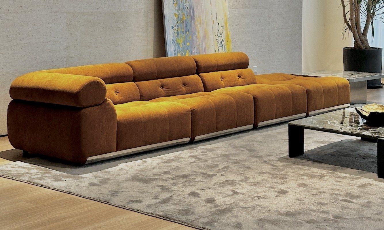 A long ochre velvet sofa with tufted cushions and a steel plinth