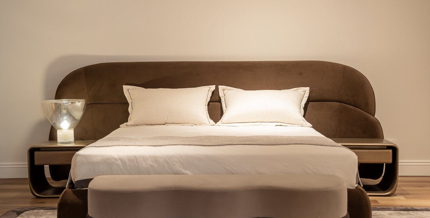 A wide brown velvet headboard with floating bedside shelves and an upholstered bench at the foot of the bed
